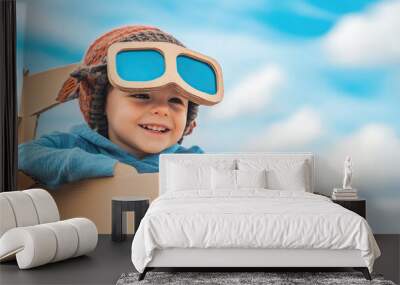 Kid boy aviator playing with cardboard airplane on sunny sky background with copy space, child diy concept Wall mural