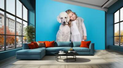 Beautiful little princess with dog. Friendship. Pets. Studio portrait over blue background Wall mural