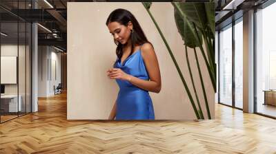 Portrait of beautiful woman fashion model brunette hair wear blue silk dress accessory jewelry earrings cosmetic face clothes for romantic date party walk summer collection tanned skin green leaves. Wall mural