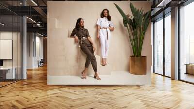 Two beautiful woman fashion model brunette hair friends wear overalls suit casual style sandals high heels accessory clothes safari Sahara journey summer hot collection plant flowerpot wall stairs. Wall mural