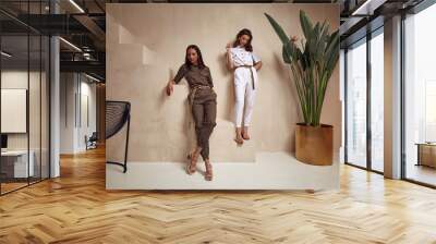 Two beautiful woman fashion model brunette hair friends wear overalls suit casual style sandals high heels accessory clothes safari Sahara journey summer hot collection plant flowerpot wall stairs. Wall mural