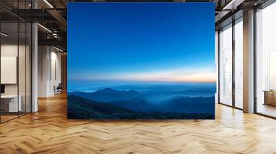 A breathtaking panoramic view of a vast mountain range at sunrise, with a clear blue sky and distant peaks bathed in golden light. Wall mural