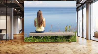 Young woman sitting on bench facing the sea Wall mural