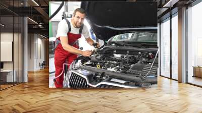 car mechanic in work clothes works in a workshop and repairs a vehicle Wall mural