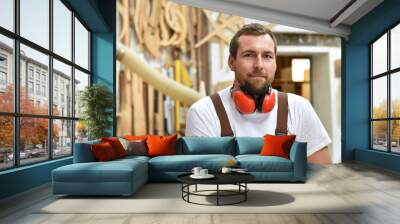 portrait of a carpenter in work clothes and hearing protection in the workshop of a carpenter's shop Wall mural