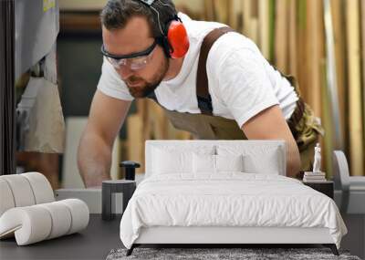 young carpenter in working clothes works in the joinery on a sanding machine - working clothes with ear protection Wall mural