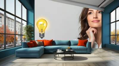 Professional woman with lightbulb floating above head on solid white background idea generation focused work environment Wall mural