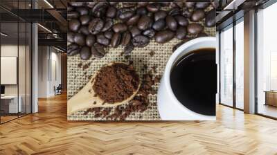 Coffee grind in wooden spoon and hot coffee on sackcloth with coffee beans background. Wall mural