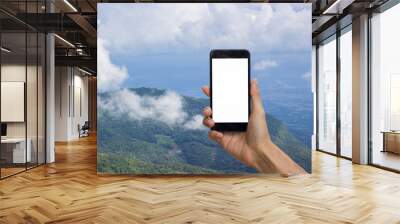 Hand holding black smartphone with white screen for mock up on top of mountain with cloud and blue as background. Wall mural