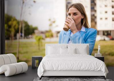 Beautiful businesswoman drinking coffee and using mobile phone while standing outdoor on a sunny day. Wall mural