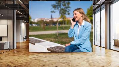 Beautiful businesswoman talking on the mobile phone while sitting on the bench outdoor. Wall mural