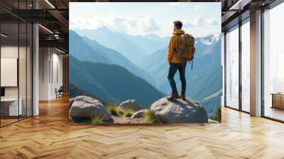 A hiker in a yellow jacket stands on a rock, admiring the panoramic view of the mountain landscape on a clear sunny day Wall mural