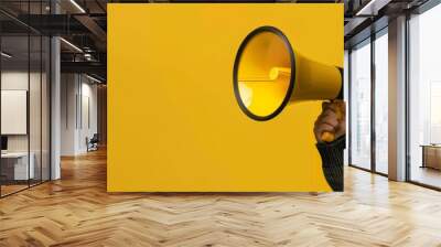 A person holding a megaphone against a bright yellow background, emphasizing the concept of making an announcement and capturing attention Wall mural