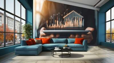 Businessman presenting digital house model on tablet with rising graphs to illustrate real estate investment growth in a modern office Wall mural