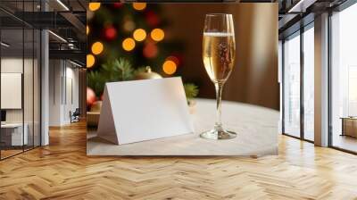 Celebratory drink and blank card on a festive table with a Christmas tree in the background during a cozy winter gathering Wall mural