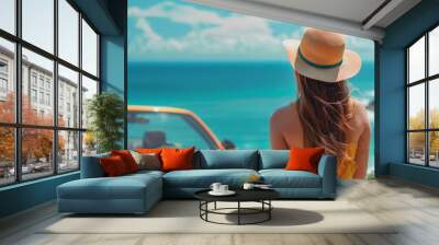 Woman with hat looking at ocean by car. Wall mural