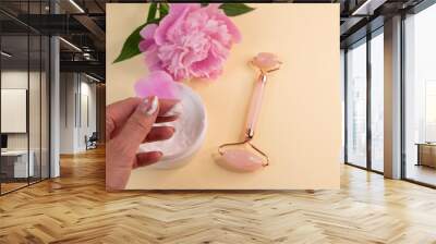 hand cream, quartz roller facial massage with pink natural jade on a background of pink peonies. Wall mural