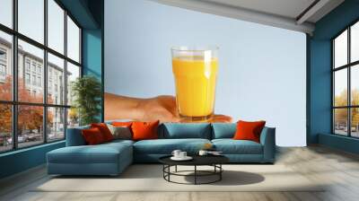 Hand holding glass of orange juice black straw isolated on blue background Wall mural