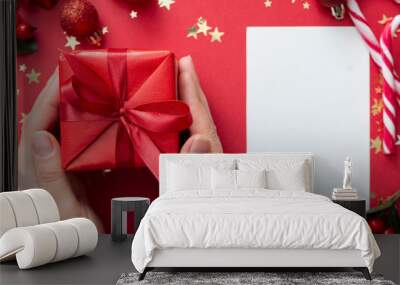 Top view of female hands holding gift box with red ribbon bow isolated over flat lay background, copy space. Wall mural