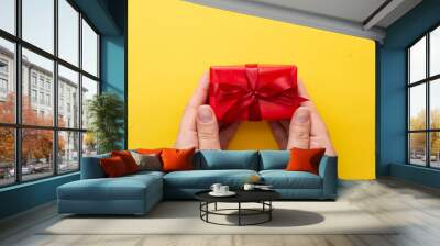 Top view of female hands holding gift red box with ribbon bow isolated over blue background, copy space. Wall mural