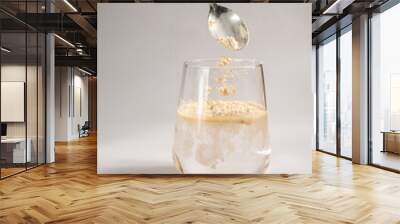 Woman pours collagen powder or protein in a glass of water on a beige background. A healthy and anti aging supplement. Copy space Wall mural