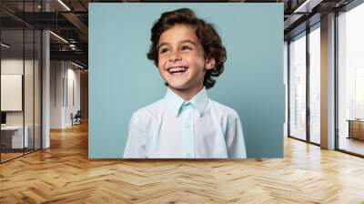 Cheerful little boy in white shirt looking at camera and smiling against blue background Wall mural