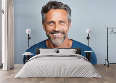 Handsome mature man in blue t-shirt smiling at camera while standing against grey background Wall mural