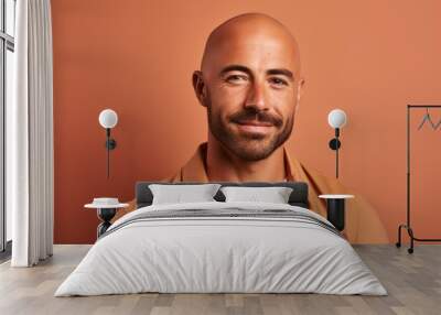 Portrait of a handsome bald man in an orange shirt on a brown background. Wall mural