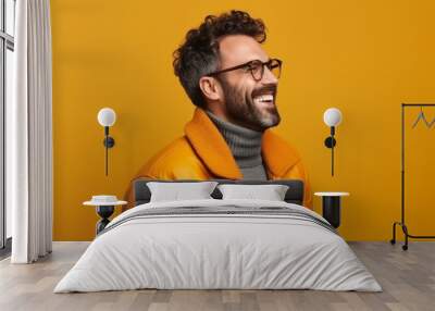 Portrait of a smiling young man in orange jacket and eyeglasses over yellow background Wall mural