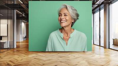 Portrait of smiling senior woman in turquoise shirt on green background Wall mural