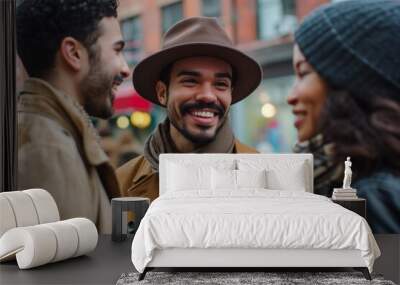 Smiling young man in hat and scarf looking at camera while walking with friends in city Wall mural