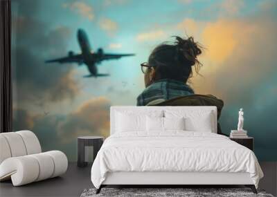 A female tourist wearing a backpack looking at airplane in the sky Wall mural