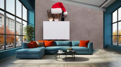 Silver knife fork and spoon with a Santa Claus red festive hat. Christmas meal background Wall mural