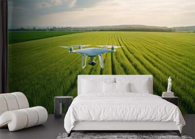 A white drone with a camera flies above a green field of grass, capturing aerial footage on a sunny day. Wall mural