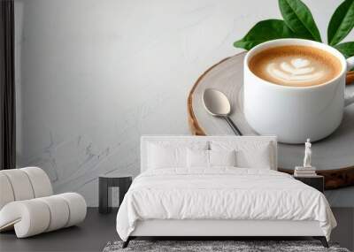 A beautifully crafted latte art in a white cup on a wooden serving board, surrounded by green leaves. Wall mural