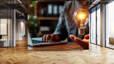 Innovative business idea concept with a person holding a glowing light bulb and working on a laptop, symbolizing creativity and innovation. Wall mural