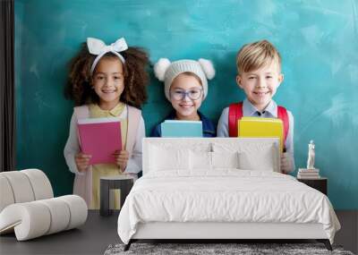 Three smiling school children holding colorful books in front of a chalkboard, ready for learning and education. Wall mural