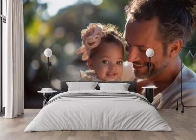 A father holds his smiling daughter in his arms, both enjoying a tender moment in a vibrant garden. The soft evening light highlights their happiness and connection Wall mural