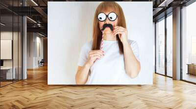 Attractive middle aged woman having fun with a fake moustache and glasses. A woman in the period of menopause.Blond / red hair mature senior female against the white wall background.Impostor syndrome Wall mural