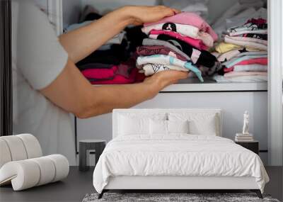 Mom picking out kid outfit at home to send her children back to school. New colored clothing stacked in a pile close-up in white wardrobe. Woman folding clothes on a shelf in a closet. Wall mural