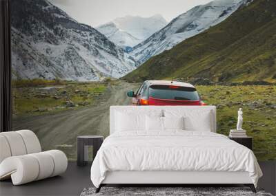 Red car on a dirt road in the mountains. Panoramic view of the dirt road among the mountains of Dagestan, Russia. Autumn landscape and highway. Mountain road among the rocks Wall mural