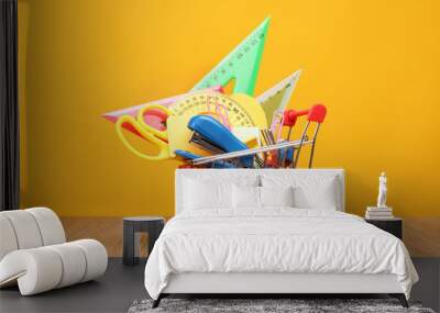 Shopping trolley with stationery on a yellow background. Wall mural