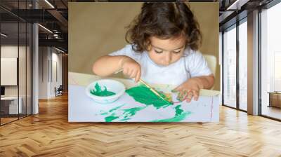 Summer or Autumn.Cute little girl drawing with green paint on fall leaves. Curly adorable child painting at table. Wall mural