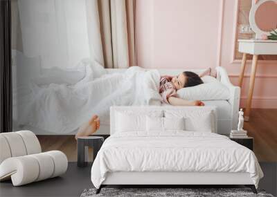 a little dark-haired girl, lying barefoot in bed. the child woke up after sleeping. good morning Wall mural