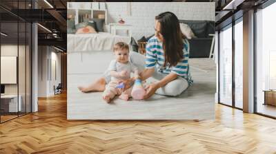 Beautiful young mother plays and teaches her baby 6 months old on the floor in the living room.mom and baby play with toys Wall mural