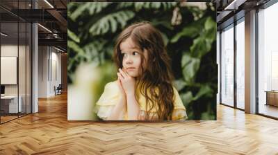 Little girl in a yellow dress in a botanical garden. a child stands near the leaves of Monstera. Wall mural