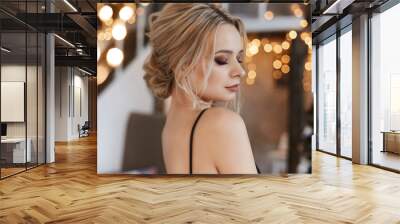 Fashionable young woman wearing luxurious evening dress and with beautiful evening makeup and hairstyle in the fairy beautiful Christmas interior. Blonde model girl with New year festive lights Wall mural