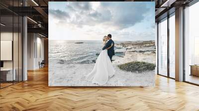 Newlywed couple hugging together on the white rocks at the seacoast at Cyprus. The bride in a wedding dress the groom in a suit posing with beautiful landscape on the background Wall mural