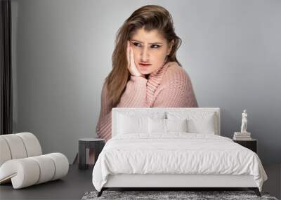 Close up portrait of a young Caucasian woman wearing a pink sweater on a grey background.  She looks sad and depressed Wall mural