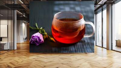 black tea in a transparent Cup next to a purple flower on a dark wooden background Wall mural